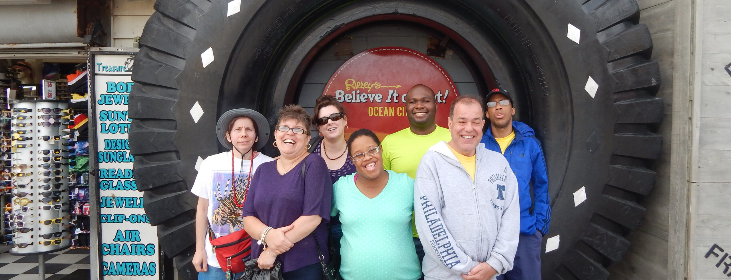 A group of seven adults gathered together in front of a sign for Ripley's Believe it or Not in Ocean City, NJ. Everyone is smiling at the camera. A boardwalk shop is visible to the left.