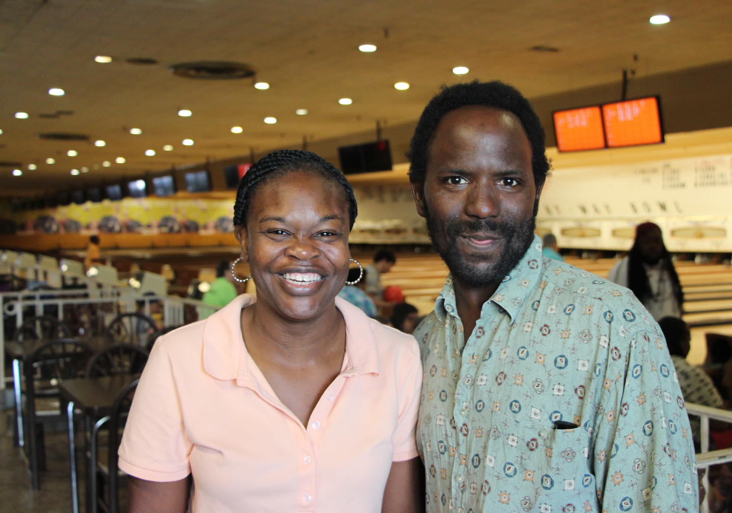 Two people standing together in a bowling alley, smiling.