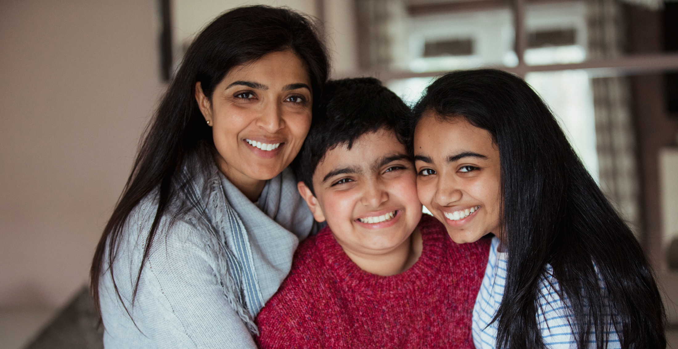 A woman and two children huddle together and smile at the camera