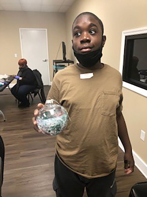 A boy in a tan shirt holding an ornament that looks like a snow globe.