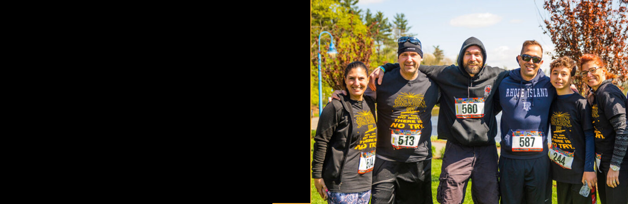 A group of six runners gathered together with their race bibs visible on their shirts. Trees and a lake are visible behind them.