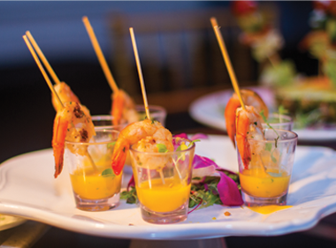 A collection of shot glasses with sauces and shrimp on skewers, sitting on a plate.